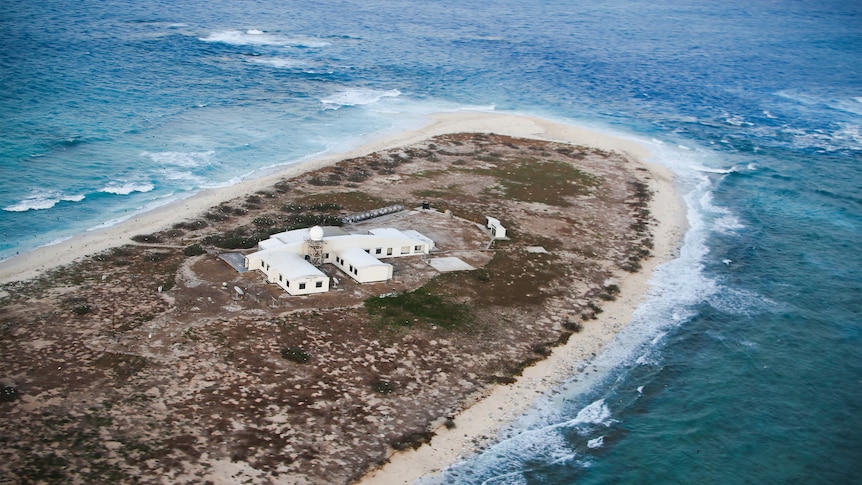 An aerial shot of a building on a tiny island surrounded by ocean