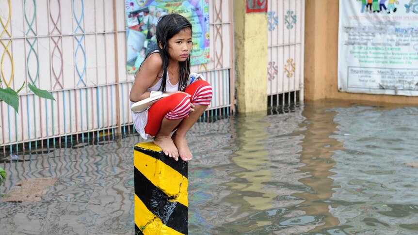 A soaking wet child sits on a post on a flooded street in suburban Manila on August 8, 2012
