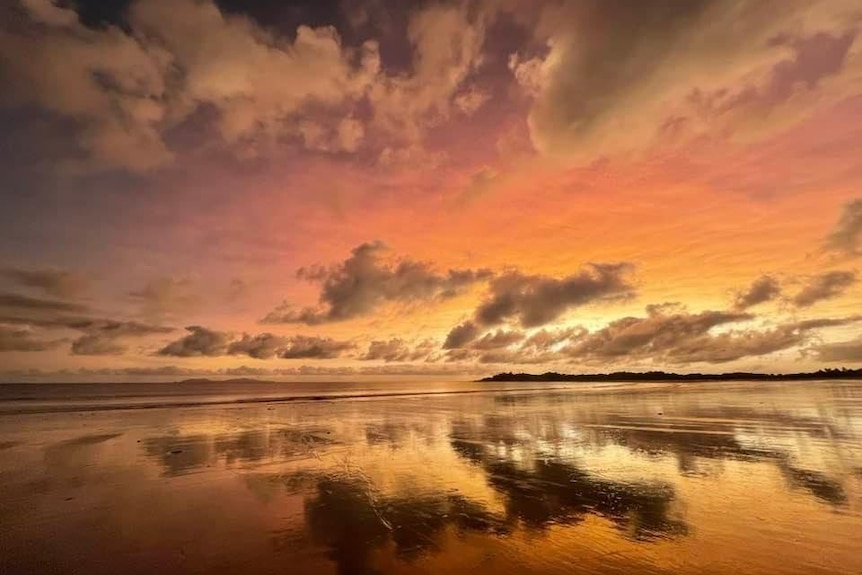 A sky with clouds at sunrise, reflecting off pools of water at the beach.