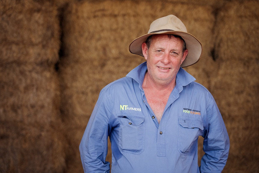 Man in blue shirt and hat standing in front of bales of cotton.