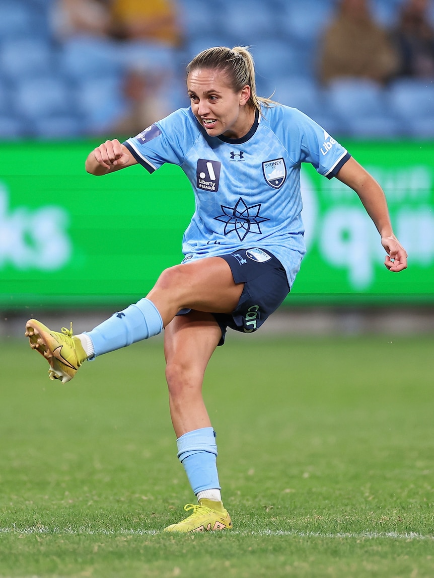 A soccer player wearing sky blue and navy kicks a ball during a match in a stadium