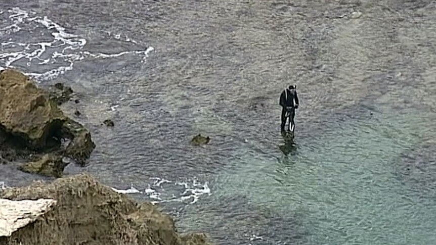 A police diver standing in the water near rocks.