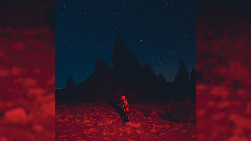 Phoebe Bridgers stands in the middle of the desert at night, wearing a skeleton suit. A red light is cast upon her.