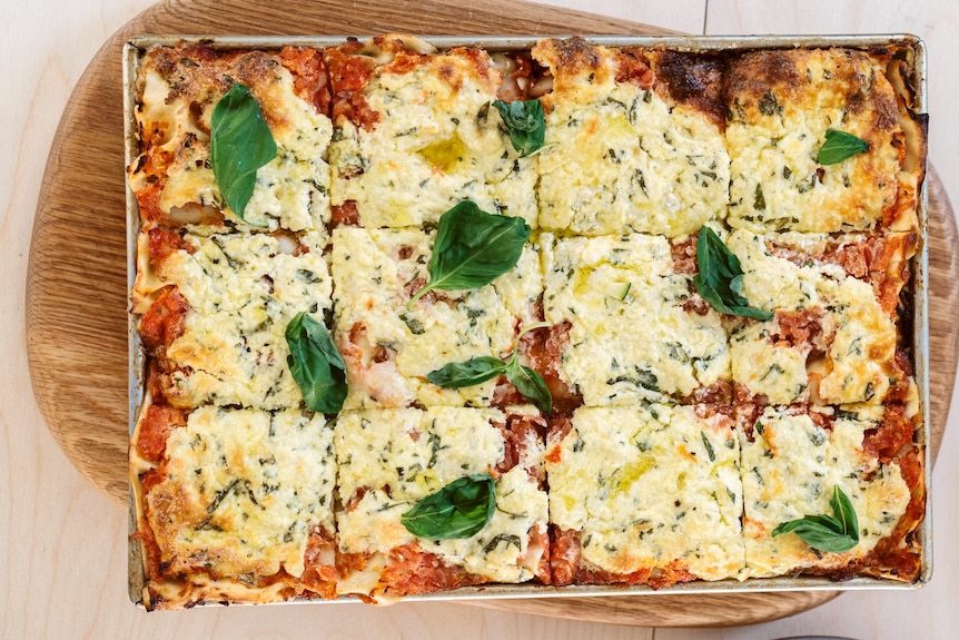 A lasagne with summer vegetables topped with cheese and basil leaves.