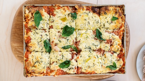 A lasagne with summer vegetables topped with cheese and basil leaves.