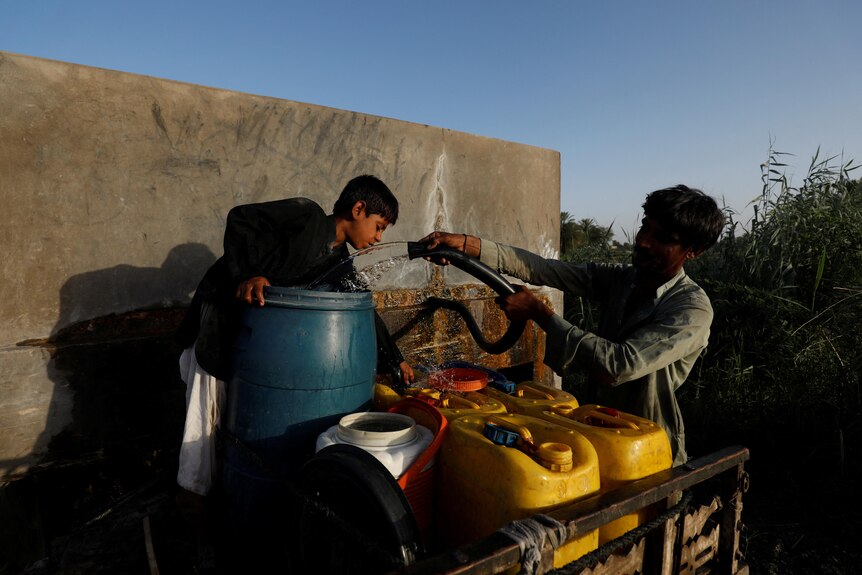 A man and his son fill water canisters from a private pump using a hose.