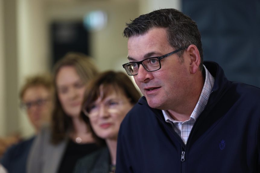 Daniel Andrews speaks to media during a press conference, with Mary-Anne Thomas out of focus behind him.