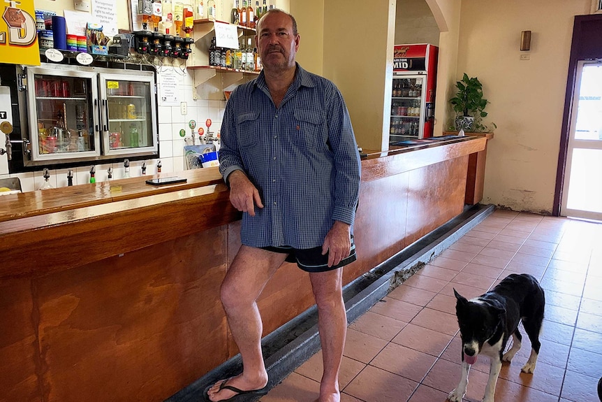 A man stands in front of a bar with pub dog