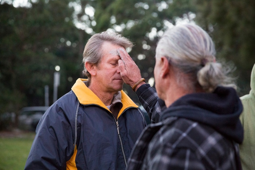 Man being blessed by person with long grey hair