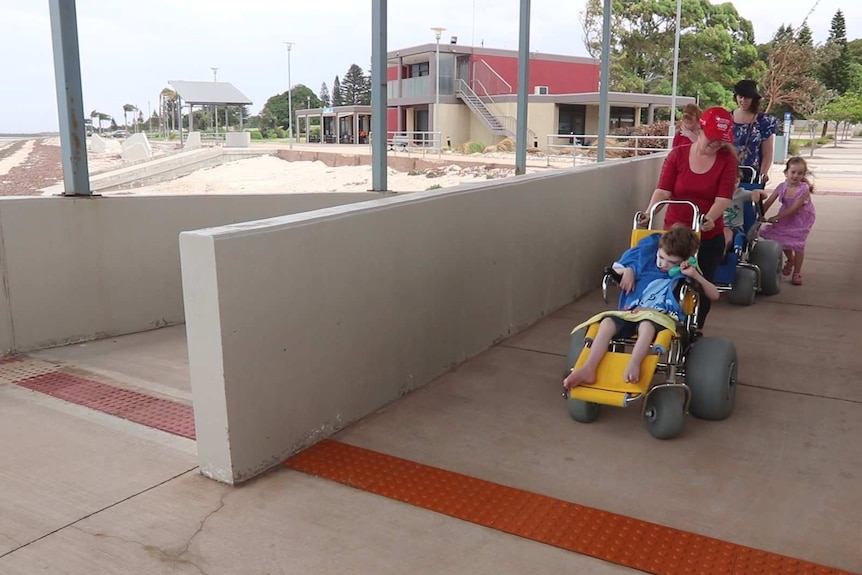 Concrete ramp structure at beach with 2 wheelchairs and mums pushing them coming down.