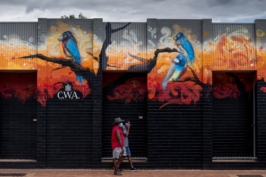 Two people walk in front of a colourful street mural in Katherine.