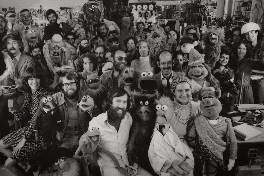 A black and white photo of Jim Henson with a sea of his Muppet creations.