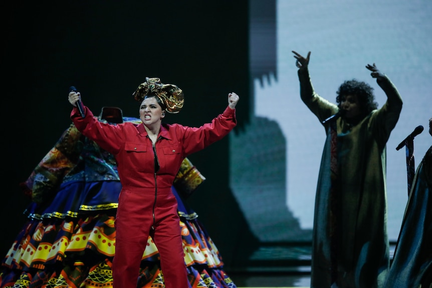 A performer in a red boiler suit dances and sings on stage at the Eurovision song contest.