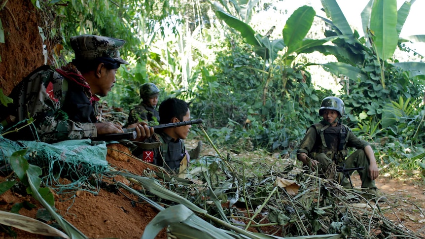 Soldiers hiding among trees holding guns. 