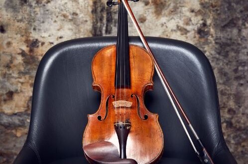 A violin sits on a black chair.