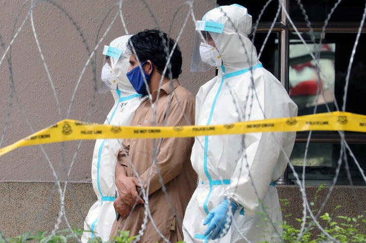 A man wearing brown is walked out of a building flanked by two police officers in masks and white hazmat suits.