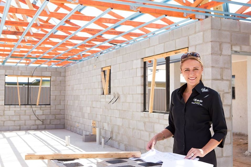 Karinda Gill stands over construction plans in the shell of building under construction.