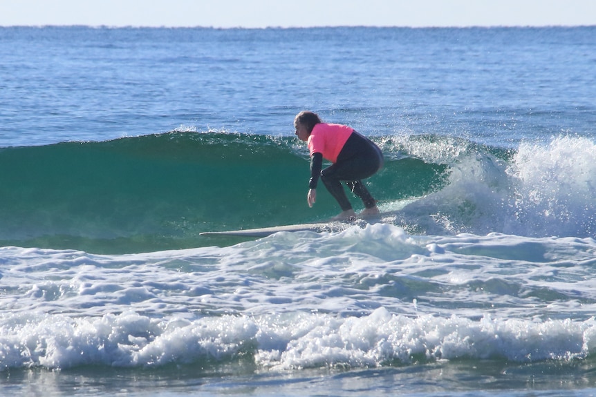 Man surfing in pink and black high vis wetsuit crouched low