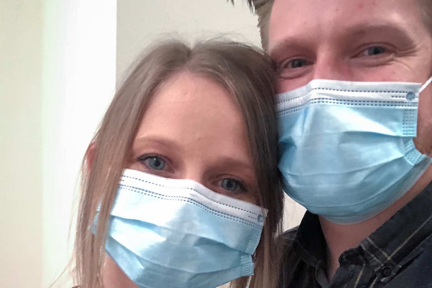 Sarah Robson and Sam Martin, both wearing protective masks, pose for a photo with their arms around each others shoulders.