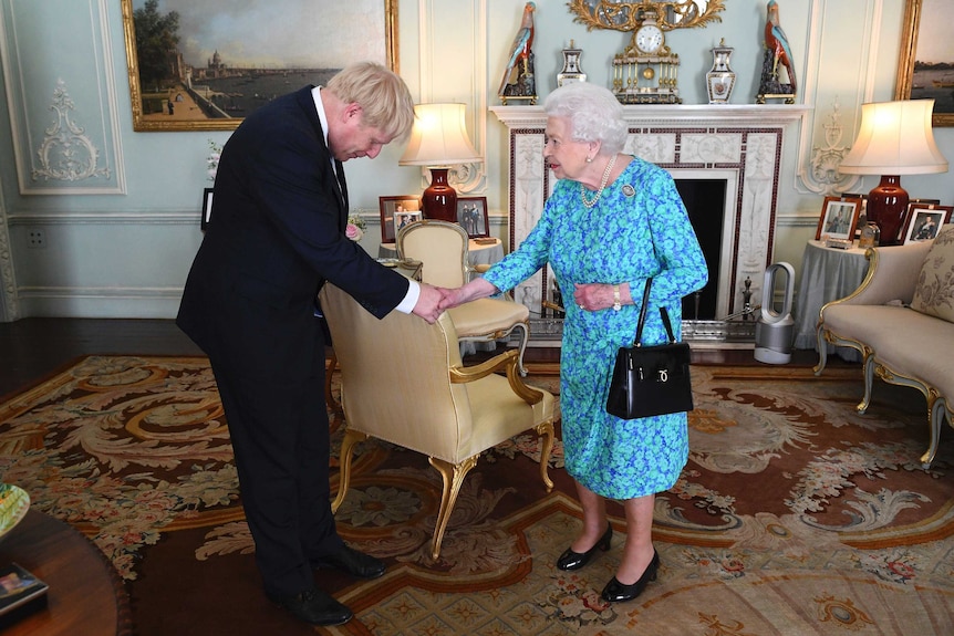 In an ornate room of Buckingham Palace, Queen Elizabeth II shakes the hand of Boris Johnson with a bowed head.