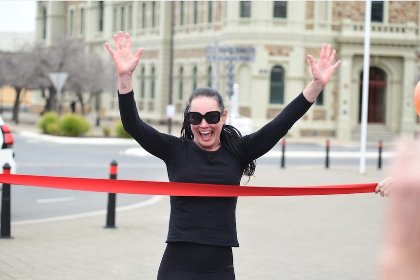 Lee-Anne Lupton smiles as she runs through red tape with her hands gleefully in the air