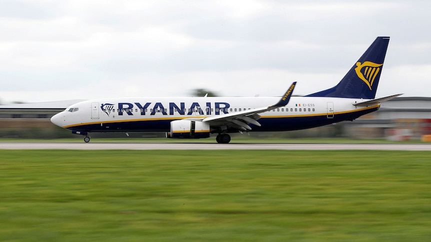 An airplane with 'Ryanair' written on its side moves along a runway with vivid rich green grass in the foreground