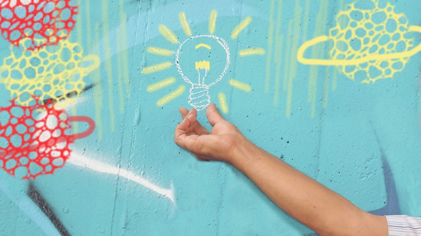 A wall painted with coloured graphics including a central light globe, with a human hand reaching up as if holding it.