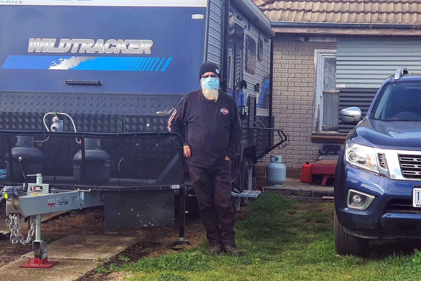 A man wears a surgical mask outside a caravan.