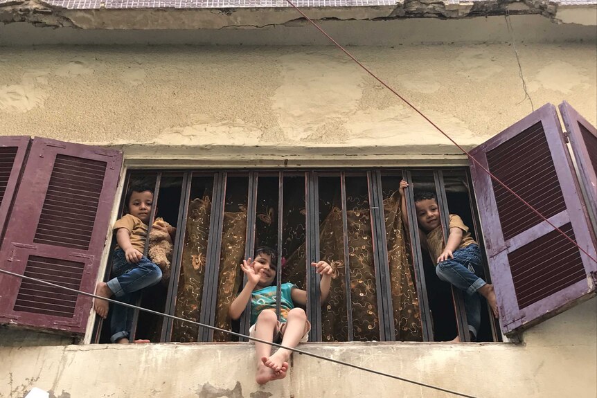 Three children hang outside the windows of an apartment in Beirut.