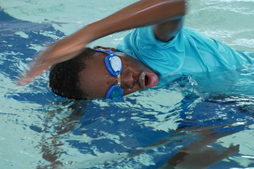 A teenage boy learns to swim in a pool