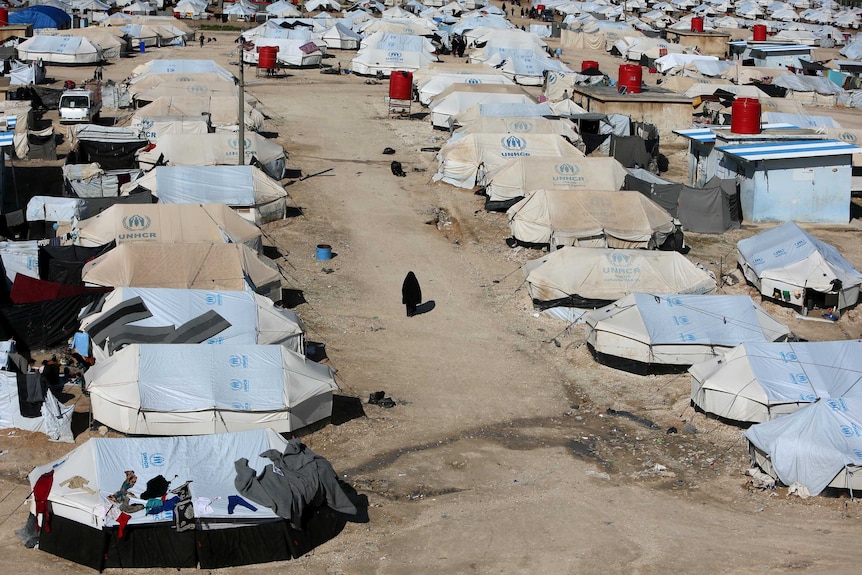 A woman in a black robe walks through a refugee camp