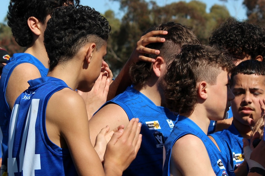 Five young men in blue singlets celebrate on the football field with pats on the back.