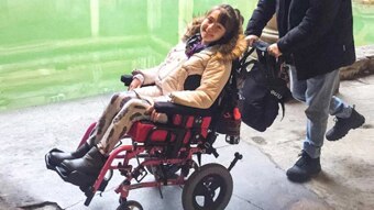 Young girl in wheelchair by Roman bath smiling at camera.