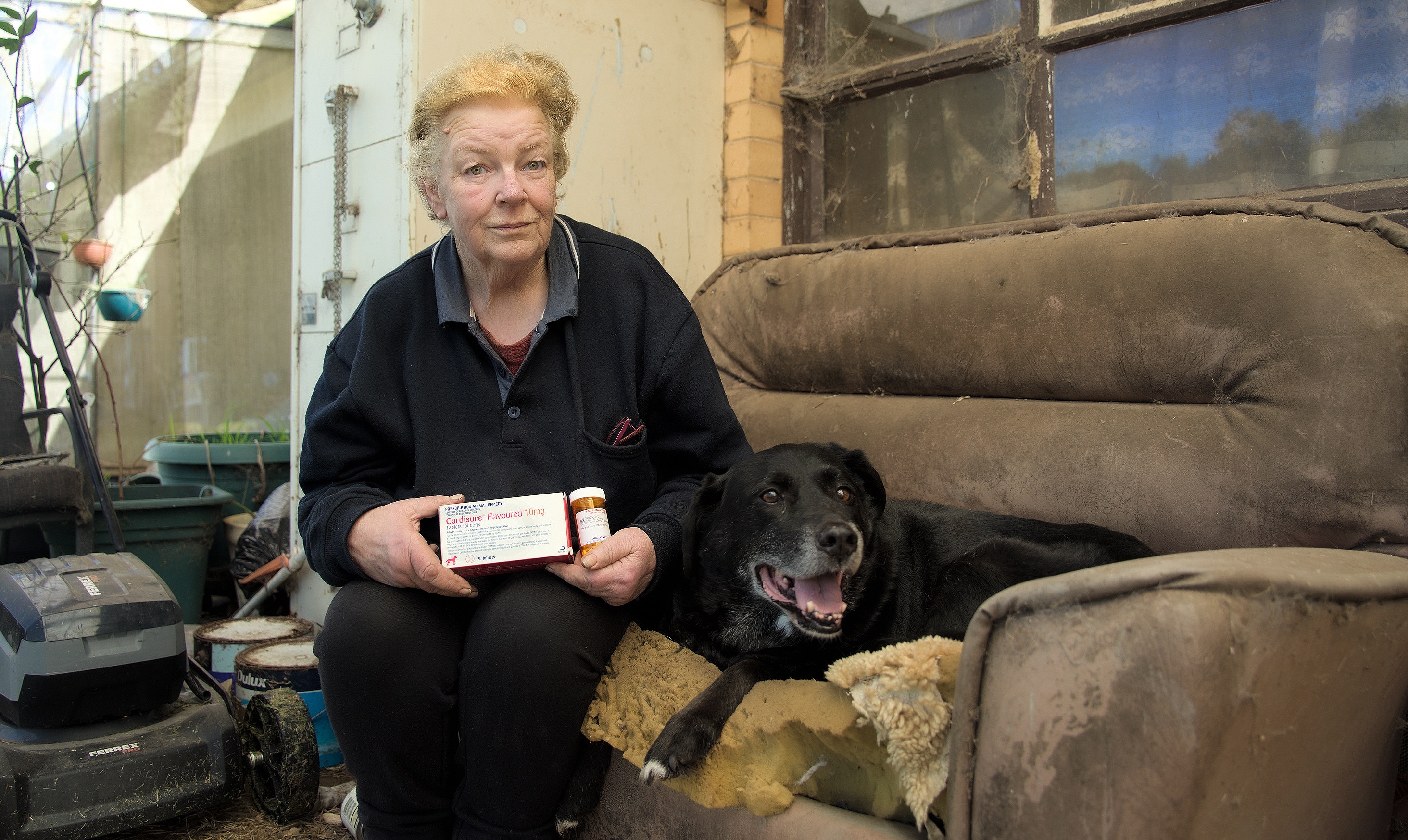 Kris holding medicine with a dog on an outdoor couch