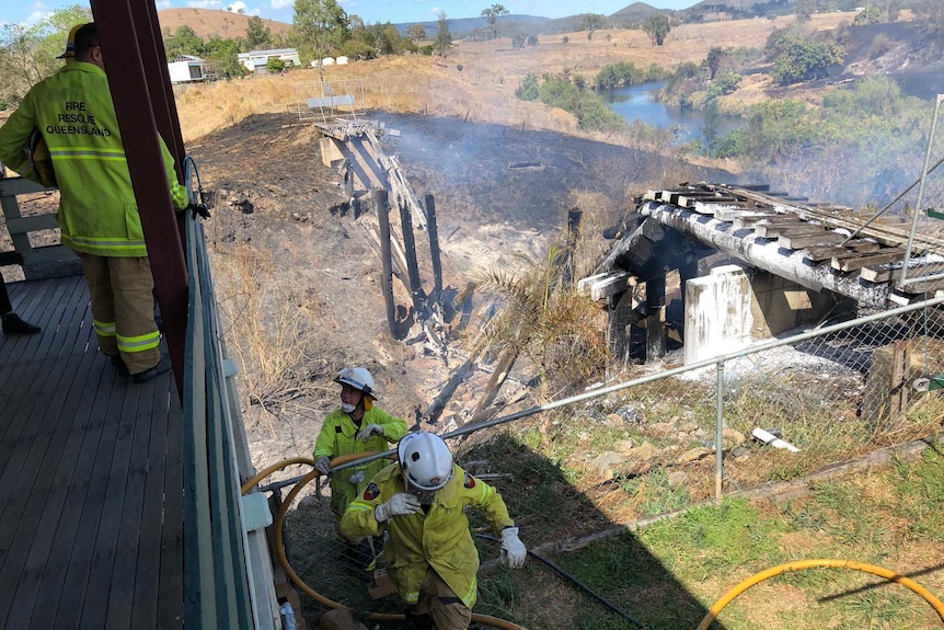 Firefighters look over the burnt out remains of a rail bridge.