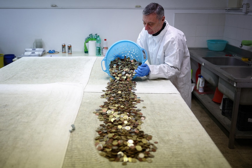 Un voluntario de Caritas descarga un cubo de monedas sobre una mesa para secarlas. 