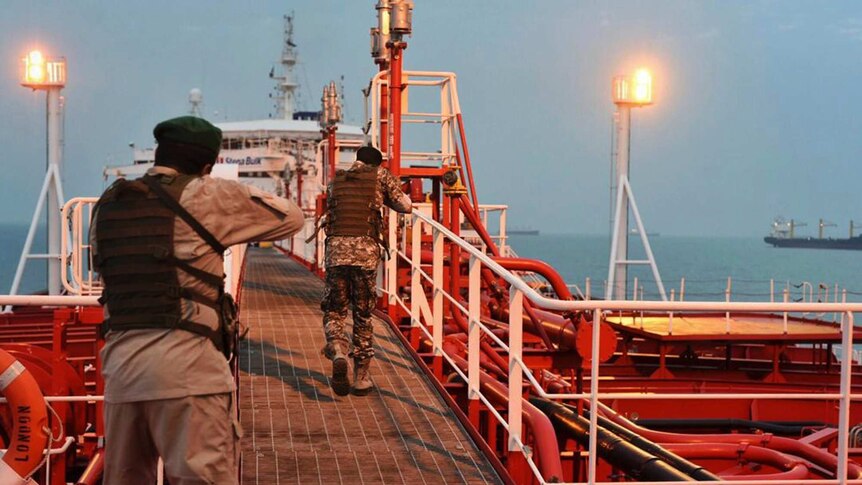 Two armed members of Iran's Revolutionary Guard walk down a passageway on a bright red ship.
