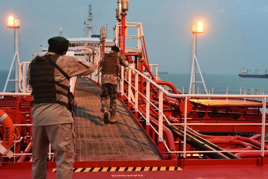 Two armed members of Iran's Revolutionary Guard walk down a passageway on a bright red ship.