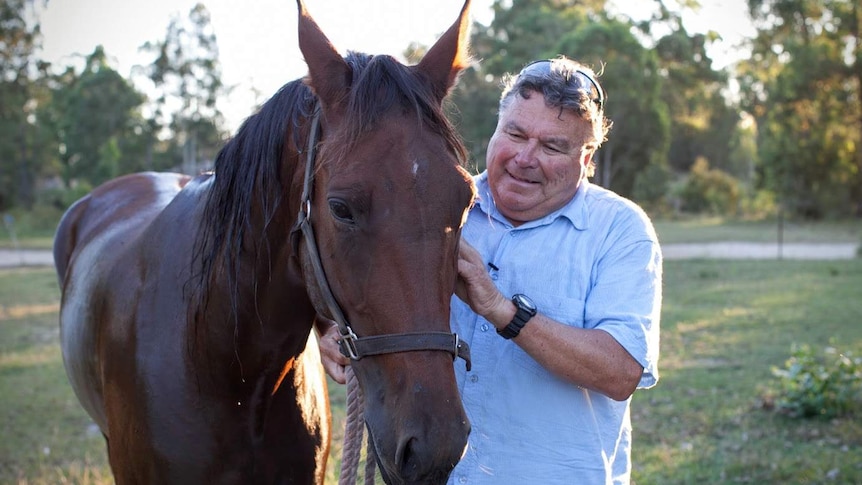 A man strokes his horse, wet after a swim.