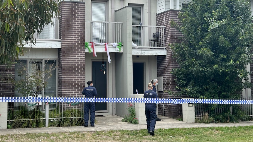 Police stand outside a townhouse which is behind police tape.