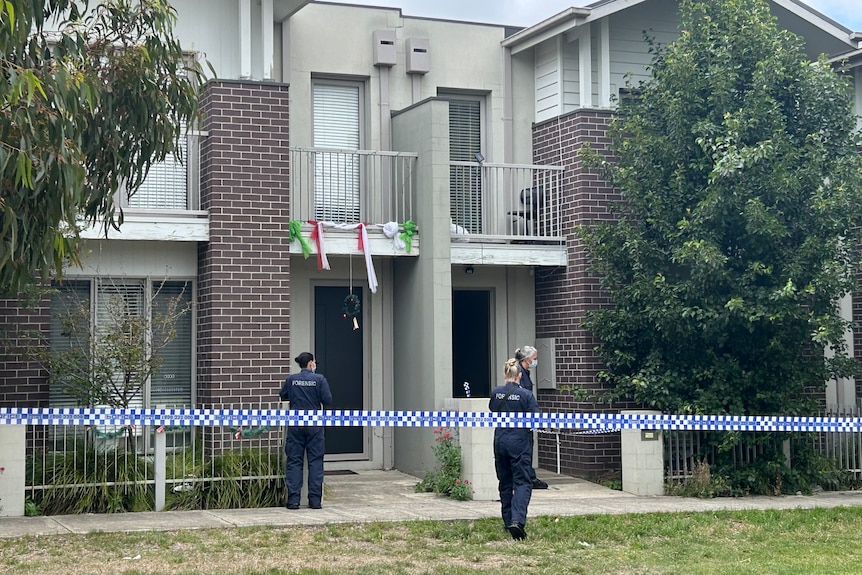 Police stand outside a townhouse which is behind police tape.