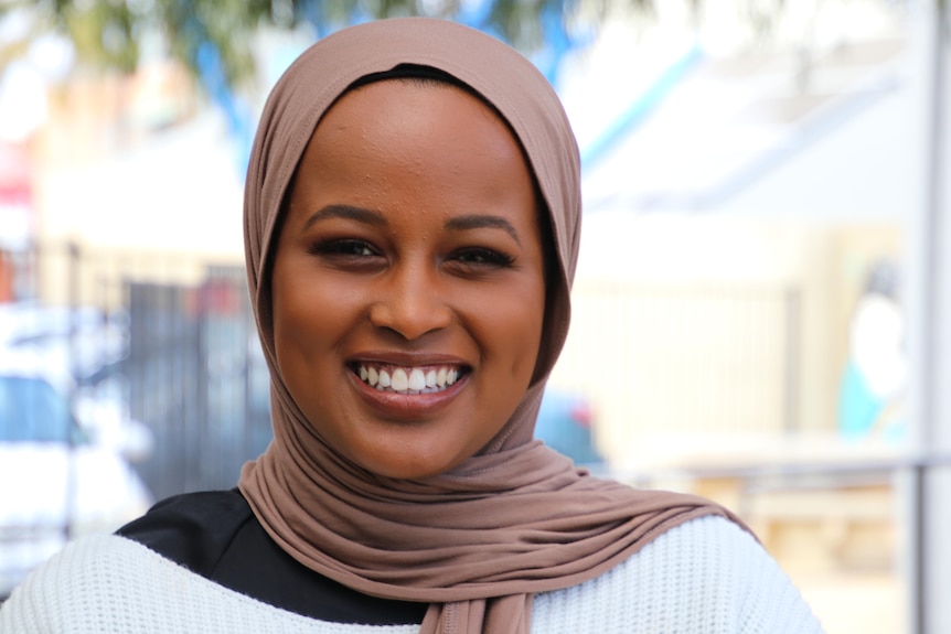 A woman smiling wearing a head scarf.