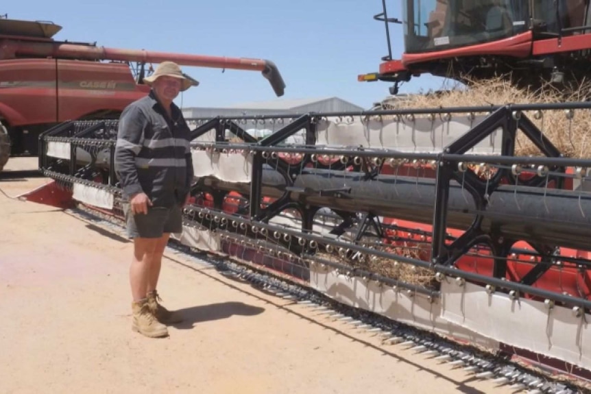 A farmer stands next to a piece of farm machinery in the paddock.