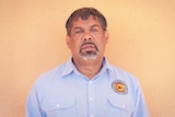 An Indigenous man in a blue collared shirt infront of an orange wall