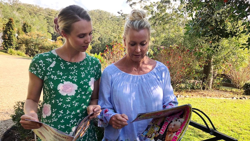 Two women standing outside, reading magazines