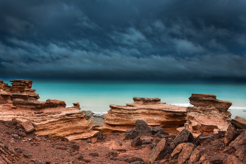 Red rocks and blue sea under stormy skies.
