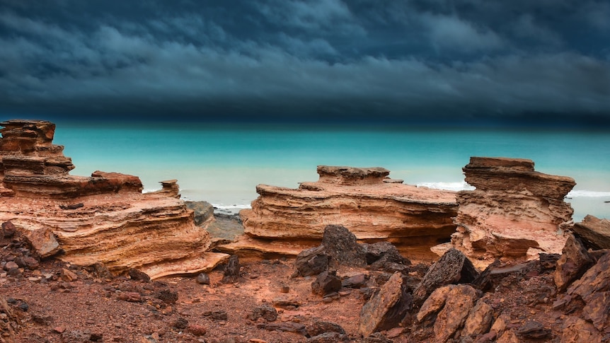 Red rocks and blue sea under stormy skies.