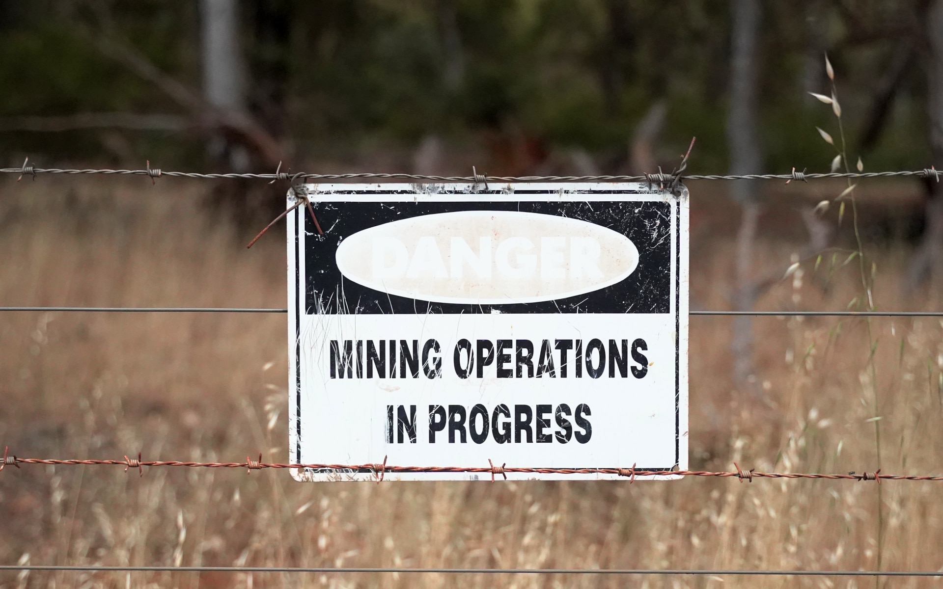 Un cartel en blanco y negro sobre una valla de alambre indica que se están realizando trabajos mineros.