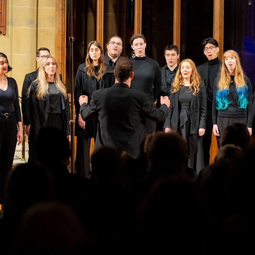 A choir dressed in black sings in a church. One siger has bright blue hair.