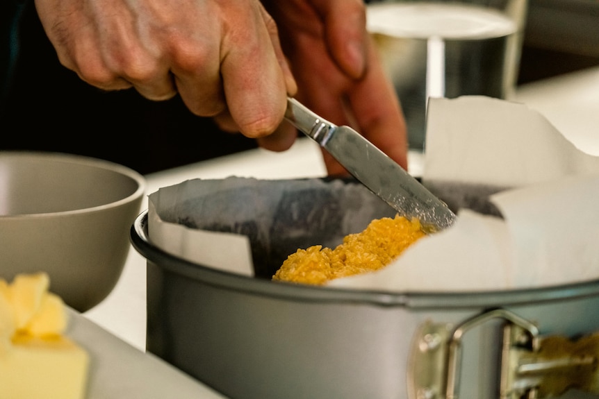 A close-up of a man's hands as he eases cake batter into a tin